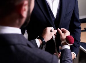 Over shoulder view of bearded fashion designer fitting bespoke suit to model, close-up shot
