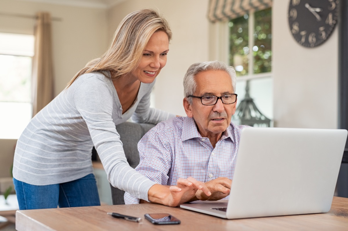 Senior man and mature daughter smiling and looking at laptop at home. 