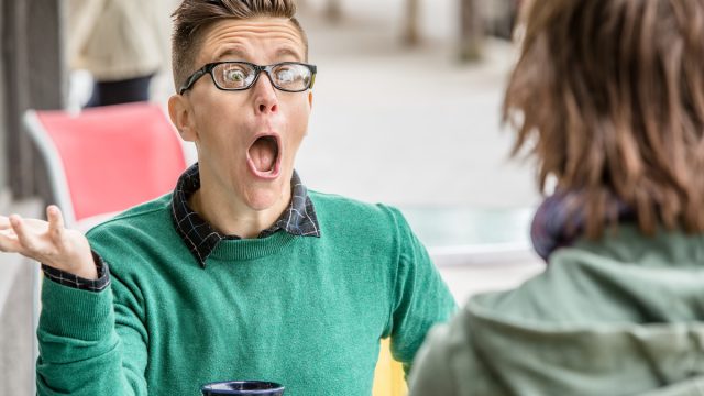 Annoying-seeming woman in green sweater talking with unidentifiable friend at outdoor restaurant