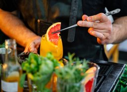Close-up of bartender putting grapefruit in a fresh cocktail in the bar