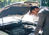 Young man looking under the hood of breakdown car