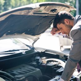 Young man looking under the hood of breakdown car