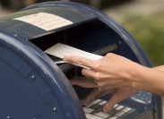 A close up of someone putting envelopes into a blue mailbox