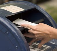 A close up of someone putting envelopes into a blue mailbox