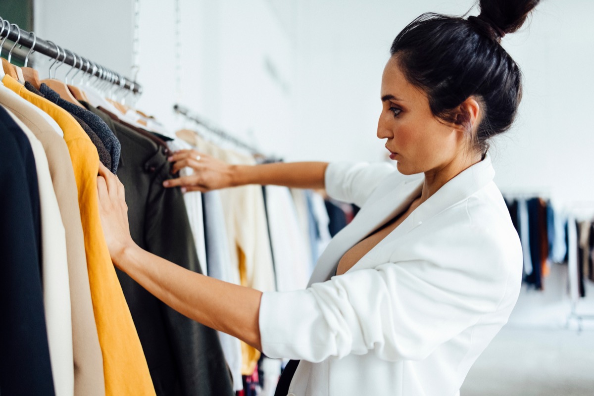 Pretty young woman standing in front of a hanger and trying to choose clothes for work or outing. Selection of wardrobe, stylist, shopping.