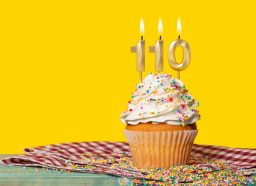 Yellow cupcake with sprinkles with 110 numbered birthday candles against yellow background