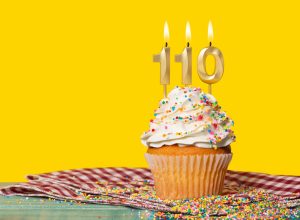 Yellow cupcake with sprinkles with 110 numbered birthday candles against yellow background