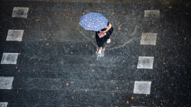 Aerial view of a woman with umbrella crossing flooded street under heavy rain