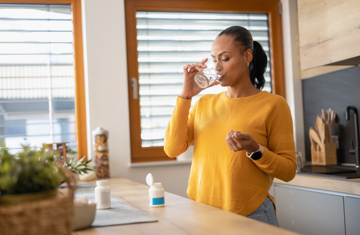 Young woman taking medicine, vitamin with water at home. Modern lifestyle and healthcare concept.