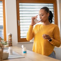 Young woman taking medicine, vitamin with water at home. Modern lifestyle and healthcare concept.