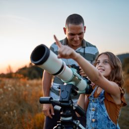 A father and his daughter looking at the sky using a telescope
