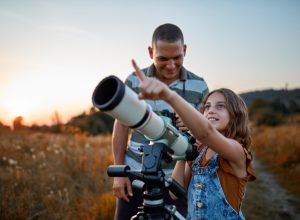 A father and his daughter looking at the sky using a telescope