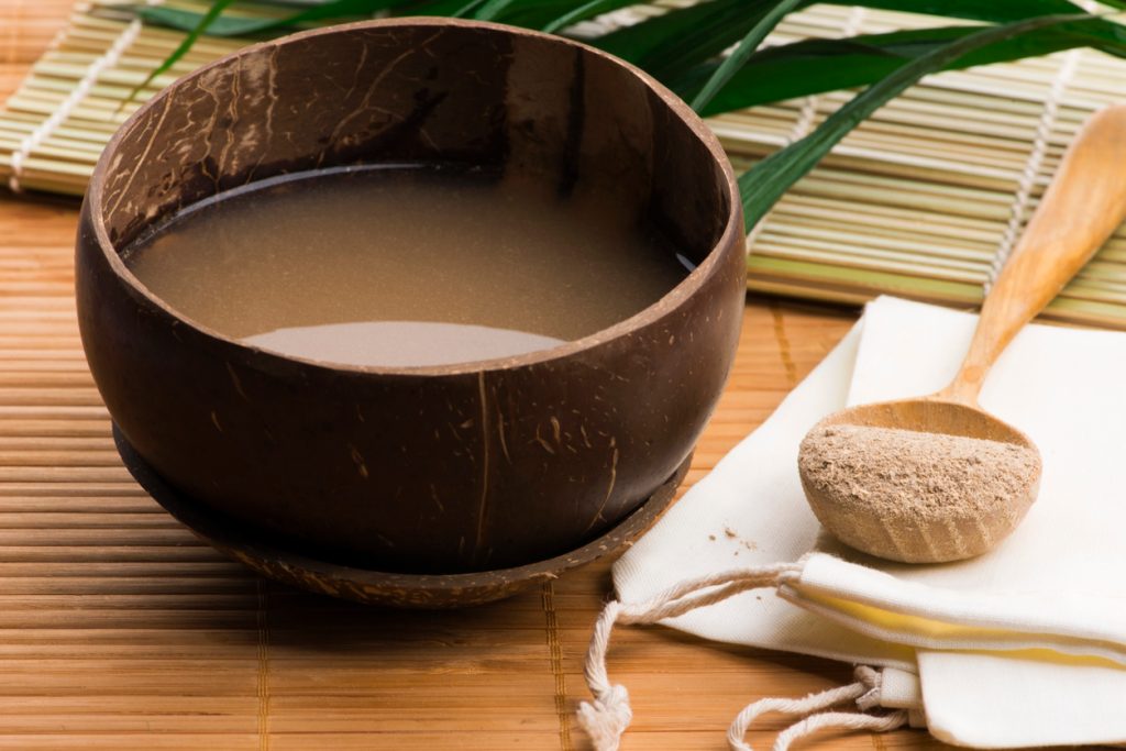 A bowl of kava root supplement in water next to a spoonful of the ground powder