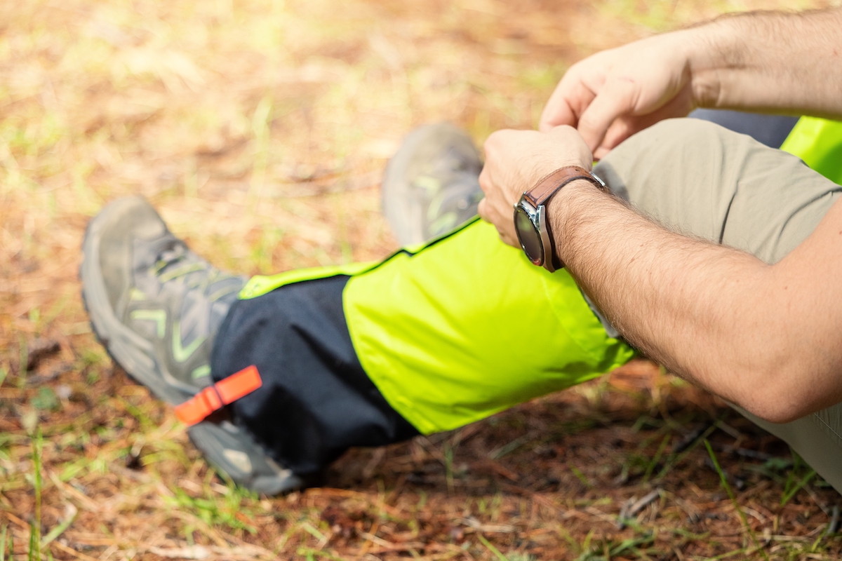 Closeup of a male hiker sitting on the ground, putting bright yellow gaiters over his hiking boots