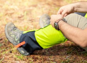 Closeup of a male hiker sitting on the ground, putting bright yellow gaiters over his hiking boots