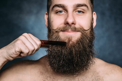 Portrait of man combing long beard; he also has a handlebar mustache