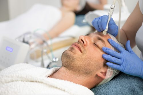 Cosmetologist treats the face of a man with microdermabrasion treatment