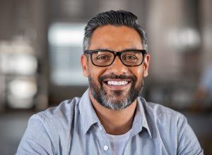 Smiling mature indian man wearing spectacles and looking at camera. Portrait of middle eastern confident businessman at office. Portrait of successful mid entrepreneur feeling satisfied and working from home.