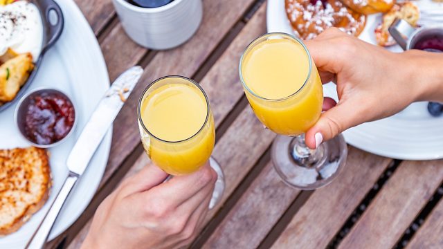 An overhead shot of two people cheersing with Mimosas at a brunch table