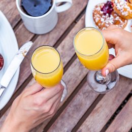An overhead shot of two people cheersing with Mimosas at a brunch table