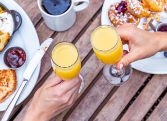 An overhead shot of two people cheersing with Mimosas at a brunch table