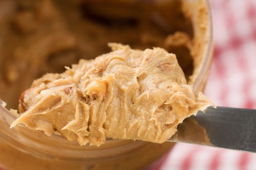 A heap of crunchy peanut butter on a knife coming out of the jar.