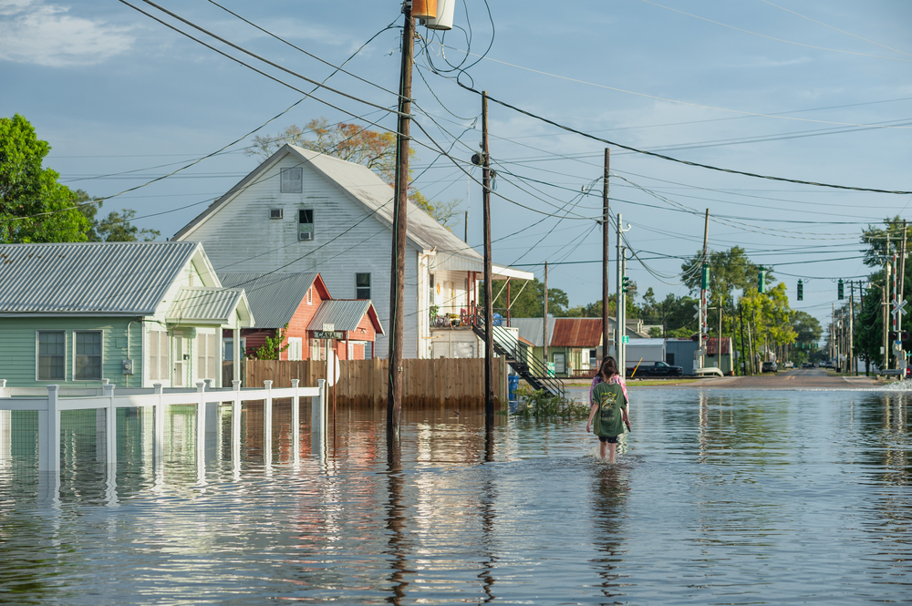 Two people walking through floodwaters next to homes