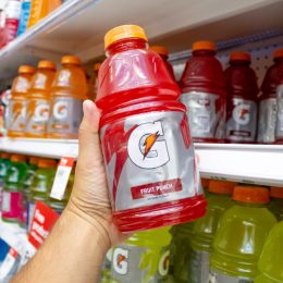 A view of a hand holding a bottle of Gatorade, on display at the grocery store.