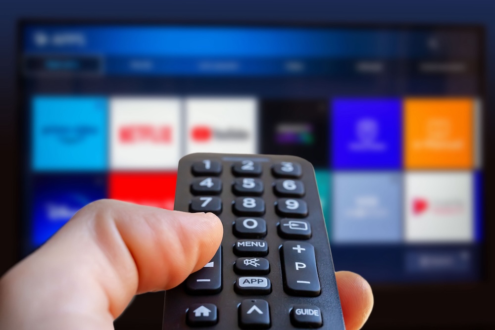 A close up of someone holding a remote and pointing it at a TV with streaming services on it