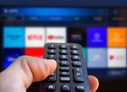 A close up of someone holding a remote and pointing it at a TV with streaming services on it