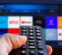 A close up of someone holding a remote and pointing it at a TV with streaming services on it