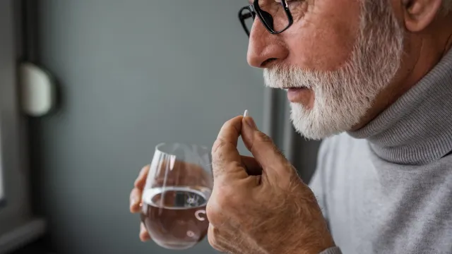 A senior man taking a supplement capsule with a glass of water