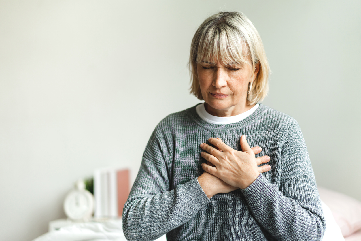 A senior woman holding her chest while sitting on her bed
