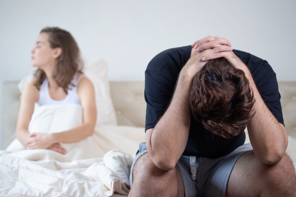 man sitting on bed with his head in hands, woman sitting in bed looking away