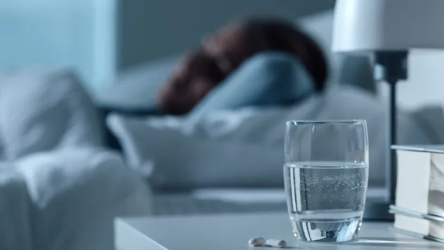 Woman sleeping in her bed at night, glass on water and pills on the foreground, medicine and treatment concept