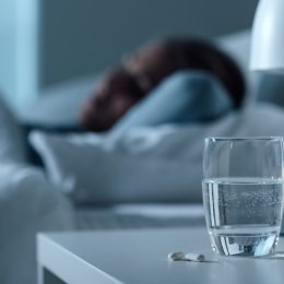 Woman sleeping in her bed at night, glass on water and pills on the foreground, medicine and treatment concept
