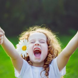 little girl with daisy in her hair making a double thumbs up and laughing at funny spring jokes