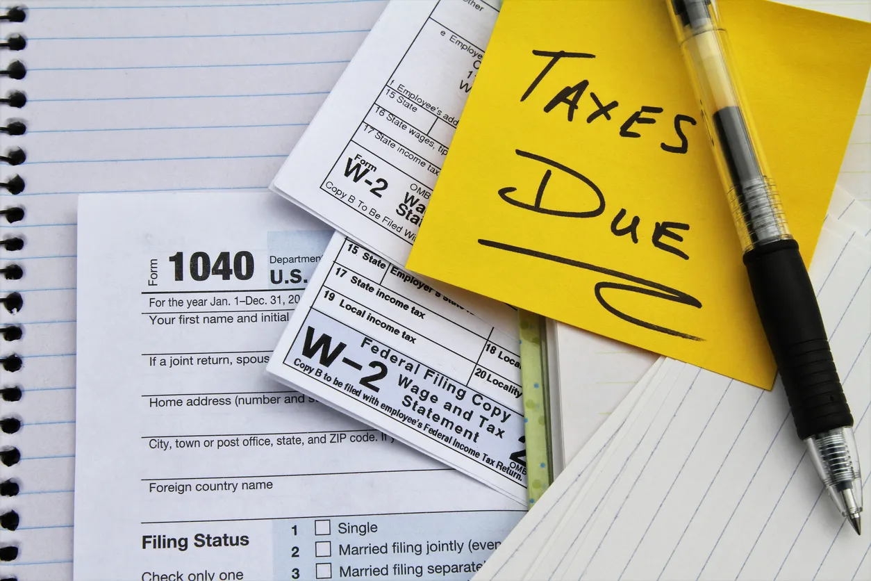 A close up of tax forms with a note on a yellow post-it that says "taxes due" on top