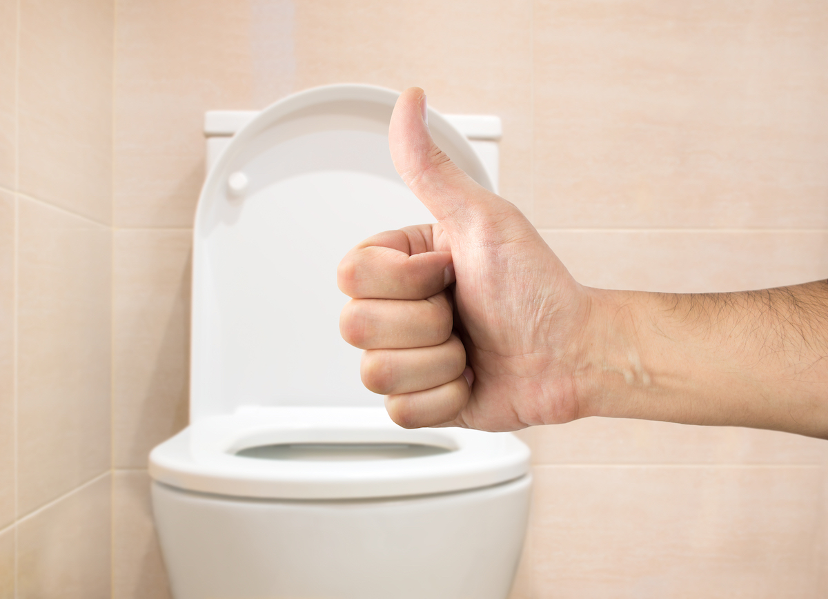 Hand making a thumbs-up sign in front of a toilet