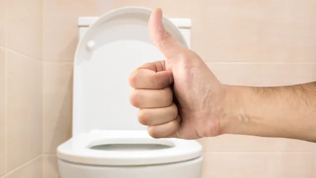 Hand making a thumbs-up sign in front of a toilet
