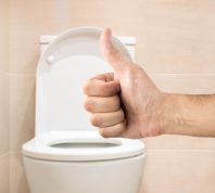 Hand making a thumbs-up sign in front of a toilet