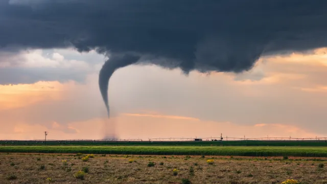 A tornado touching down in a field with a dark cloud above it