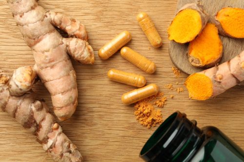Aromatic turmeric powder, raw roots and pills on wooden table, flat lay