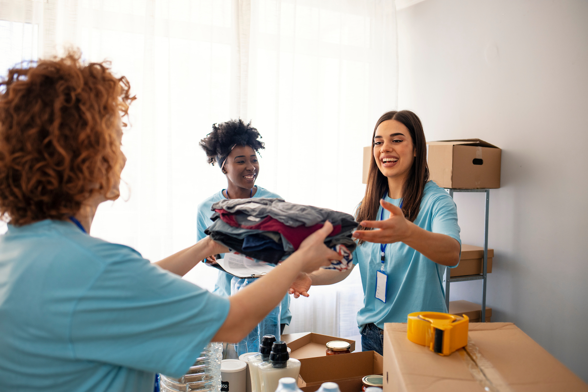 Three female volunteers wearing light blue t-shirts collecting donated clothing