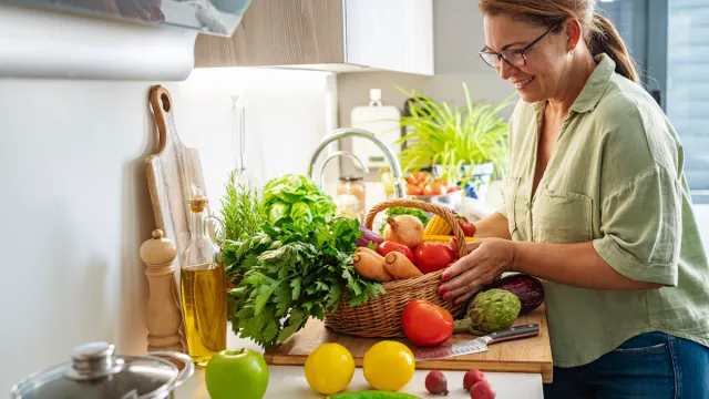 Woman with basket full of fresh vegetables in kitchen