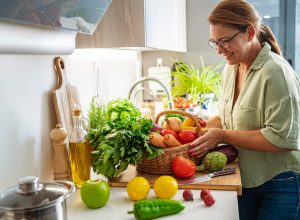 Woman with basket full of fresh vegetables in kitchen