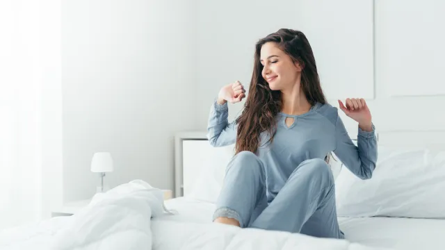 Woman in blue pajamas stretching in bed