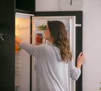 Happy woman opening the fridge and taking food from the upper shelf