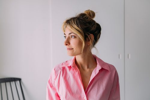 Side profile of a woman in a pink shirt. She has dirty blonde hair pulled into a messy bun.