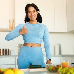 Happy woman in blue workout clothes giving a thumbs up in her kitchen
